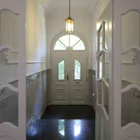 Heller Hausflur mit Doppeltür, Marmorboden und klassischer Deckenleuchte im Altbau.